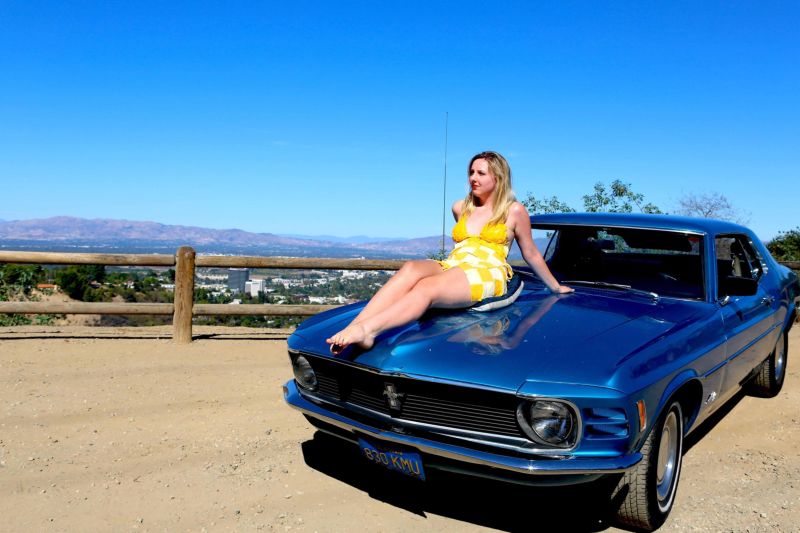 Девушки, одетые в сыр, фотографируются на фоне старых тачек